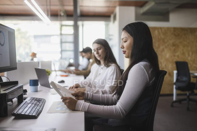 Багаторасові колеги-жінки аналізують схеми за столом під час роботи в сучасному робочому просторі — стокове фото