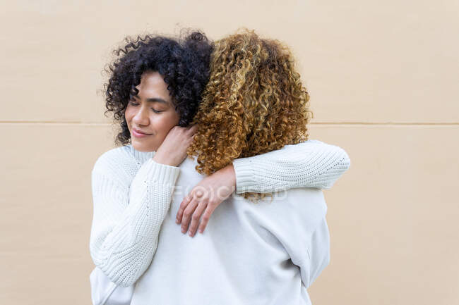 Vue arrière de femme anonyme embrassant petite amie calme à la fois avec les cheveux bouclés debout sur la rue — Photo de stock