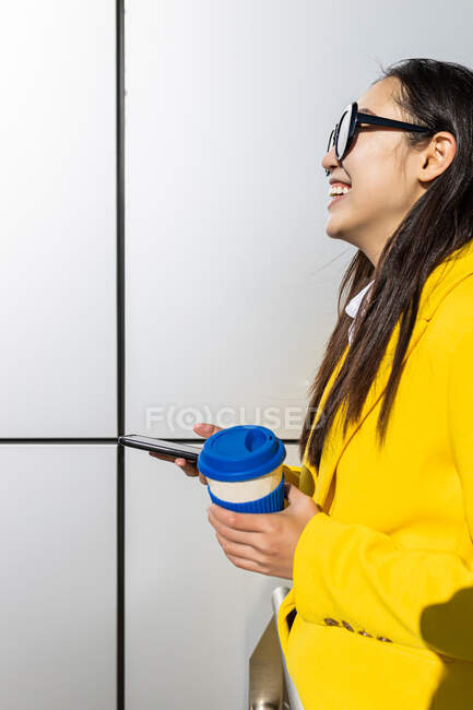 Femme d'affaires asiatique avec manteau jaune et téléphone intelligent avec fond métallique — Photo de stock