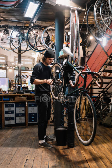 Junge Facharbeiter reparieren Detail am Rad des Fahrrads, das während Wartungsarbeiten in der Werkstatt hängt — Stockfoto