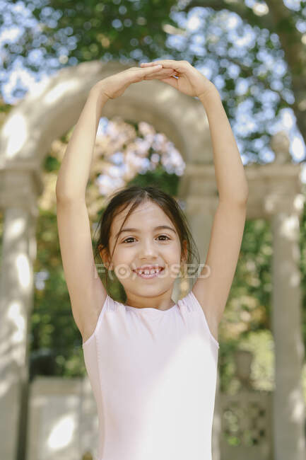 Entzückte bezaubernde Teenager-Balletttänzerin, die mit erhobenen Armen im Sommergarten auftritt und in die Kamera schaut — Stockfoto