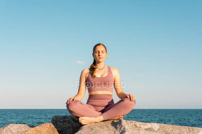 Serena fêmea com os olhos fechados fazendo ioga em pose de lótus durante a meditação na rocha na praia — Fotografia de Stock