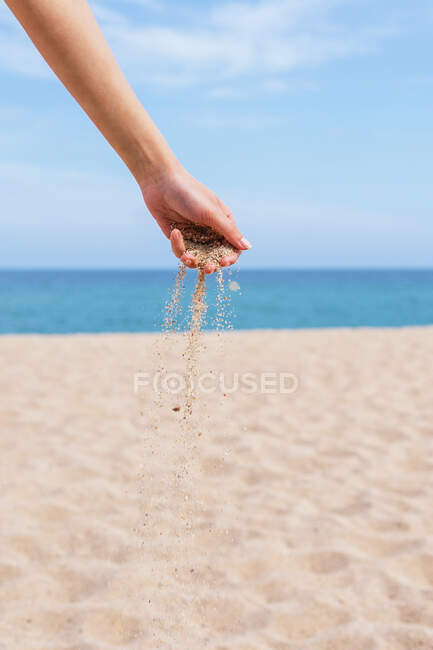 Анонимная самка с горсткой песка, бегущей сквозь пальцы, стоящие на берегу моря летом — стоковое фото