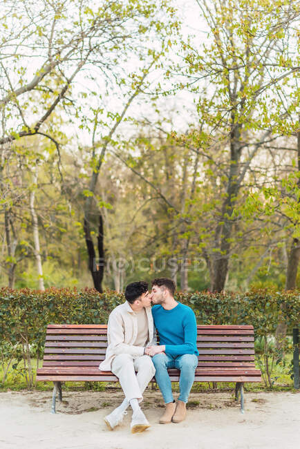 ЛГБТ пари чоловіків сидять на лавці в парку і цілуються під час освячення рук — стокове фото