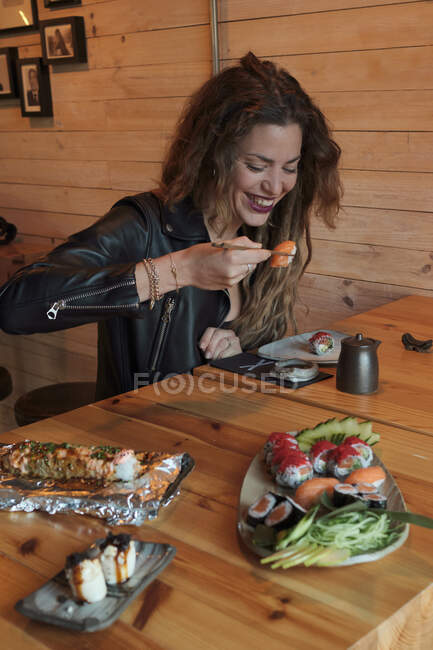 Sonriente hembra comiendo sushi sabroso en el restaurante japonés mientras está sentado en la mesa de madera - foto de stock
