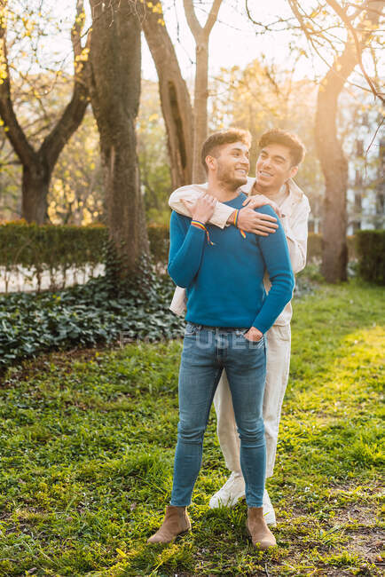 Cheerful LBGT couple of men embracing while standing in park and looking at each other — Stock Photo