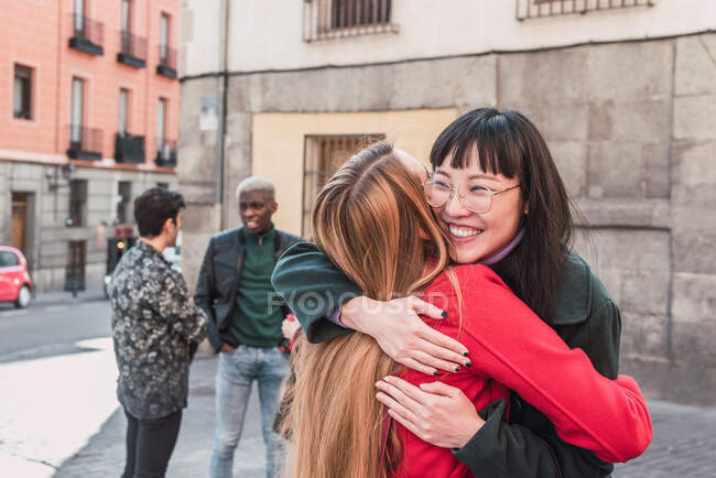 Захоплені багаторасові друзі-жінки обіймаються, стоячи на міській вулиці і насолоджуючись вихідними — стокове фото