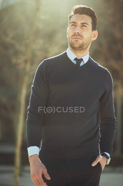 Empreendedor masculino barbudo em relógio de pulso com corte de cabelo moderno olhando para longe na cidade em volta iluminado — Fotografia de Stock