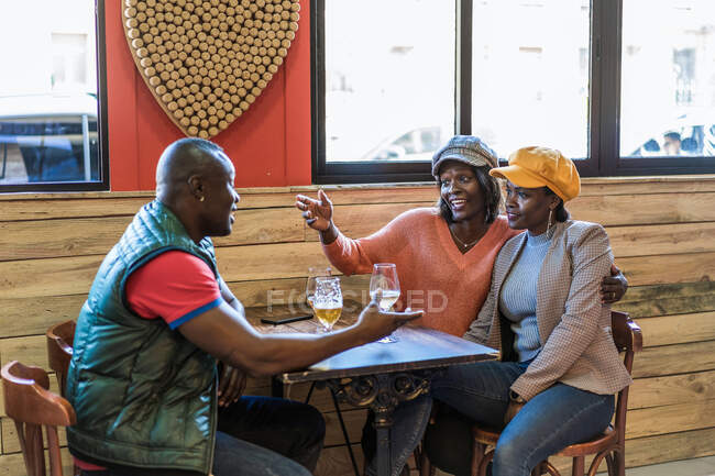 Compagnia di contenuti Amici afroamericani che si riuniscono a tavola con la birra al bar e parlano tra loro — Foto stock