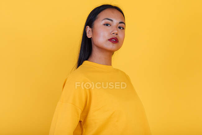 Портрет азіатської жінки, що стоїть на жовтому тлі в студії, дивлячись на камеру — стокове фото