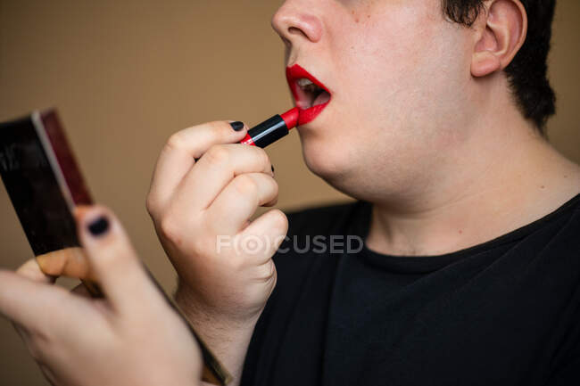 Feminine androgynous man with curly hair applying lipstick on lips while doing makeup — Stock Photo
