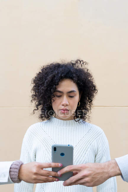 Faceless diverse people holding smartphone in front of young ethnic woman with curly hair — Stock Photo