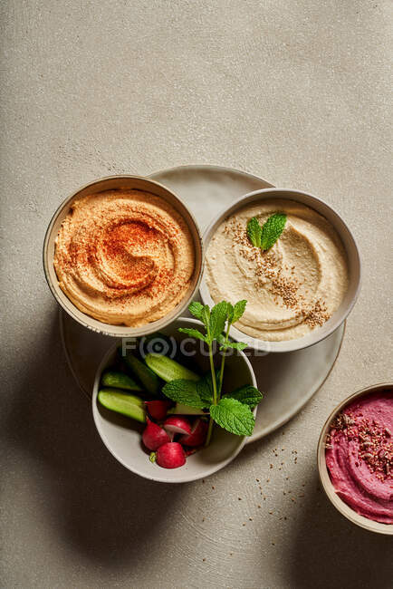 Top view of bowls with assorted hummus served on table with fresh cucumbers and radish — Stock Photo