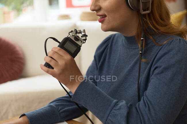 Зворотний бік нерозпізнаної жінки в навушниках записує подкаст, розмовляючи в мікрофоні і використовуючи ноутбук вдома. — стокове фото