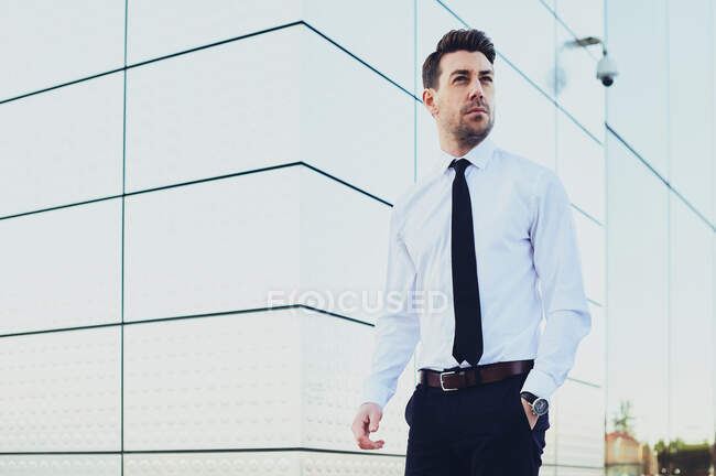 Hombre emprendedor en ropa formal con reloj de pulsera mirando hacia otro lado en la ciudad - foto de stock
