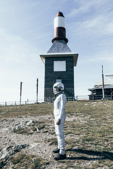 Ganzkörper-Mann im Raumanzug steht an sonnigen Tagen auf felsigem Boden gegen Metallzaun und gestreifte raketenförmige Antennen — Stockfoto