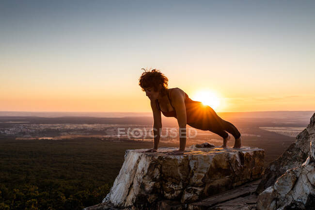 Молода йогиня практикує йогу на скелі в горі зі світлом сходу сонця — стокове фото
