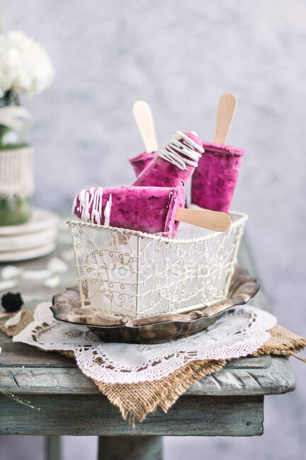Cesta branca de gelo com deliciosos picolés de iogurte de amora na tela na mesa rústica — Fotografia de Stock