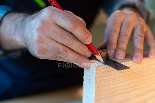 Crop professional woodworker with pencil and measuring tool making marks on timber board while creating handicraft object in carpentry workshop — Stock Photo