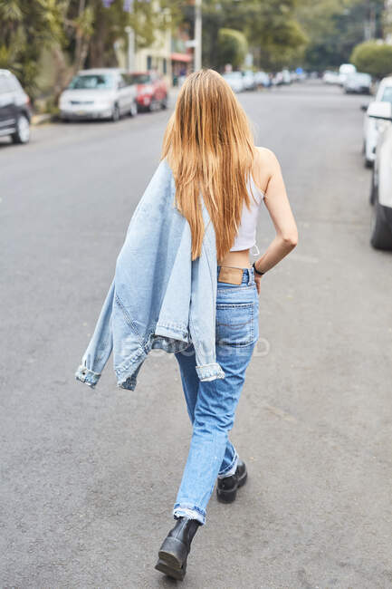 Back view of young female in sunglasses and denim clothes laughing in street while enjoying weekend and looking at camera — Stock Photo