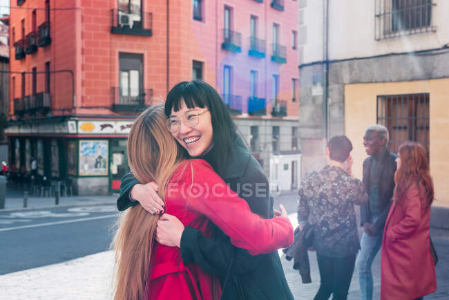 Восхитительные многорасовые подруги обнимаются, стоя на городской улице и наслаждаясь выходными. — стоковое фото
