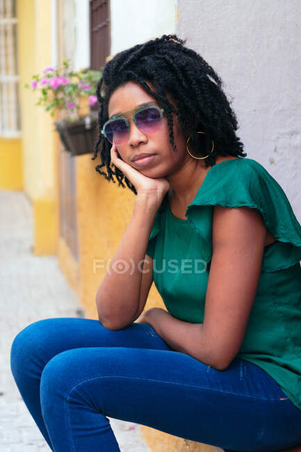 Retrato de una hermosa mujer afroamericana sentada en la calle. Concepto urbano. - foto de stock