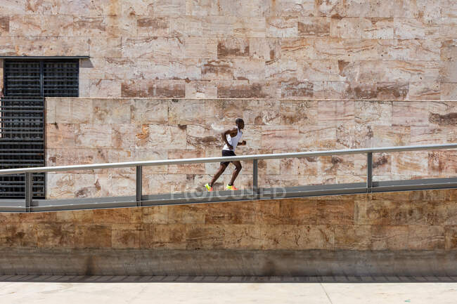 Vista laterale dell'atleta afroamericano di sesso maschile che corre lungo la costruzione di metallo in strada durante l'allenamento attivo — Foto stock