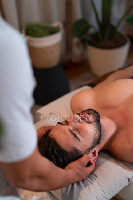 Desde arriba masajista de cultivos anónimos haciendo masaje tailandés para el cliente masculino en el moderno salón de spa - foto de stock