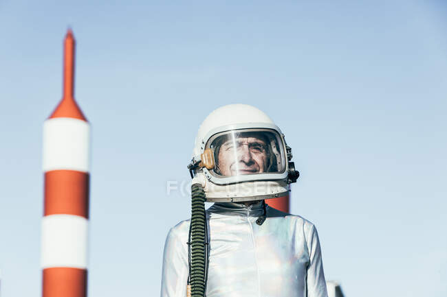 Homem em traje espacial em pé em solo rochoso contra antenas em forma de foguete listrado no dia ensolarado — Fotografia de Stock