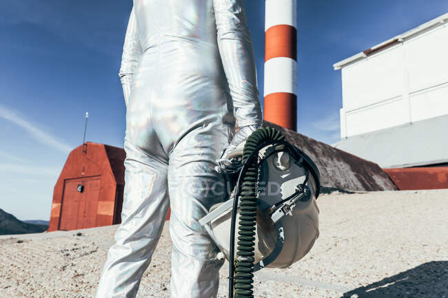 Vista posterior de un traje espacial de pie en suelo rocoso contra las antenas en forma de cohete rayado en el día soleado - foto de stock