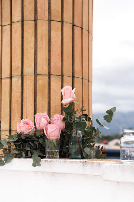 Розовые розы внутри стеклянных ваз размещены на террасе на открытом воздухе — стоковое фото