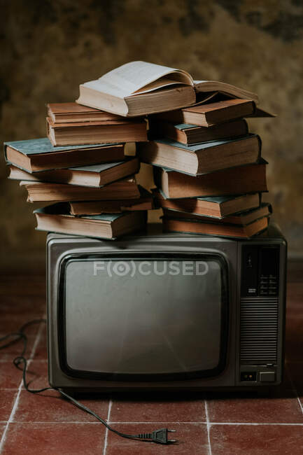 Куча книг, помещенных поверх старинного телевизора на потрепанном кафельном полу — стоковое фото