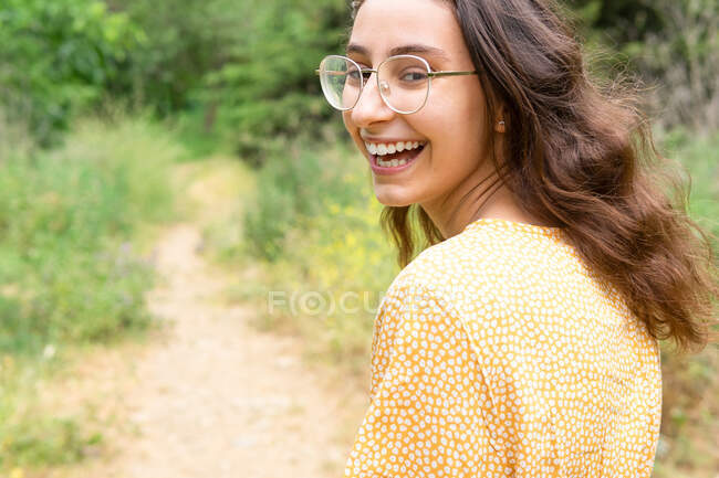 Back view of delighted female in dress walking in park and looking at camera over shoulder in summer — Stock Photo
