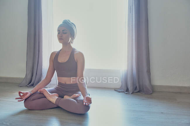 Mulher consciente sentada com pernas cruzadas e olhos fechados enquanto pratica ioga no chão em sol — Fotografia de Stock