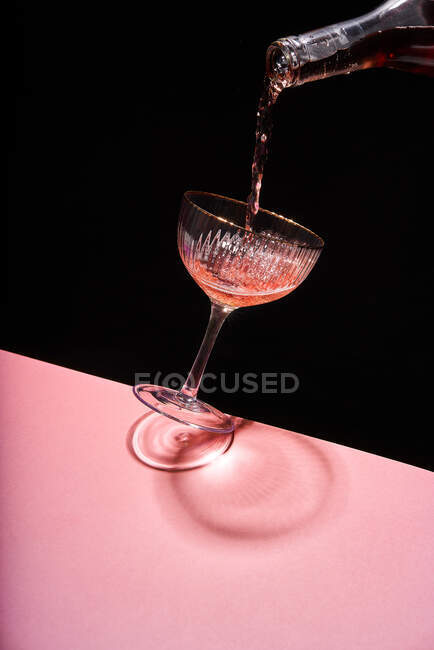 Anonyme Person schenkt Rosensekt in elegantes Coupé-Glas vor zweifarbigem Hintergrund ein — Stockfoto