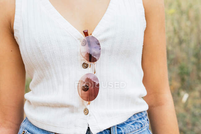 Crop view of an anonymous woman with sunglasses hanging from her shirt — Stock Photo