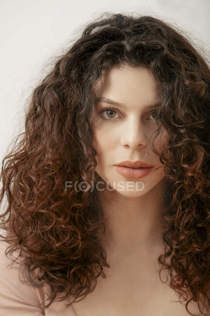 Sério feminino com cabelos cacheados olhando para a câmera no fundo branco no estúdio — Fotografia de Stock