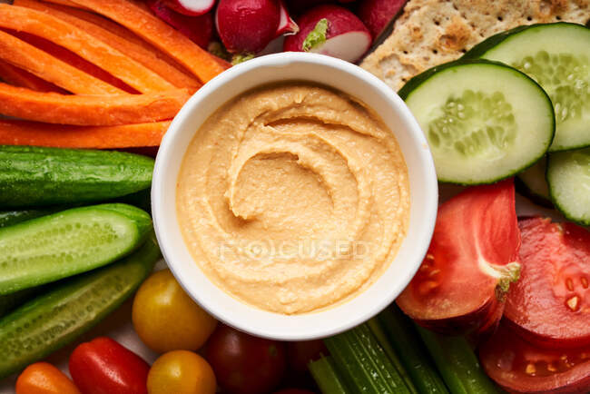 Top view bowl of homemade hummus served on plate with assorted fresh colorful vegetables — Stock Photo