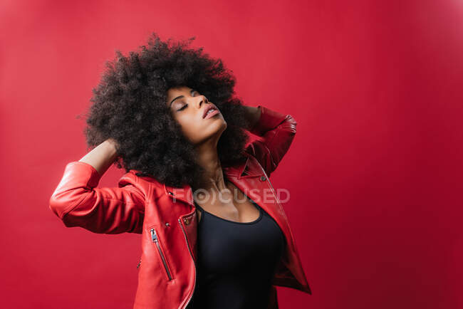 Naughty African American female screaming and touching hair on red background in studio — Stock Photo