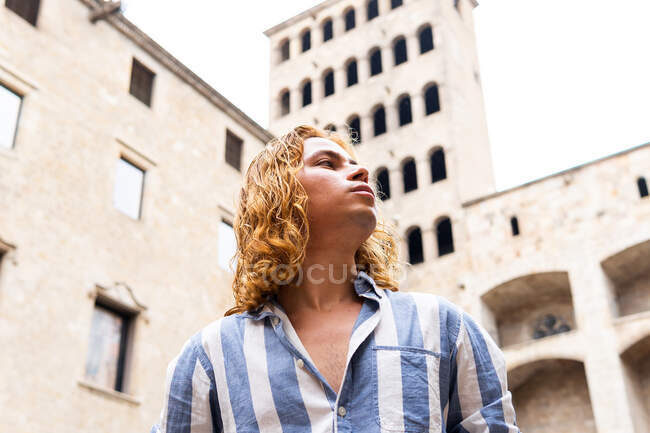 From below peaceful unemotional male with long hair standing in street and enjoying freedom while looking away — Stock Photo
