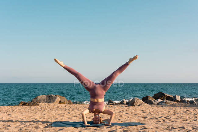 Relaxed female balancing in Salamba Sirsasana on mat while doing yoga on seashore — Stock Photo