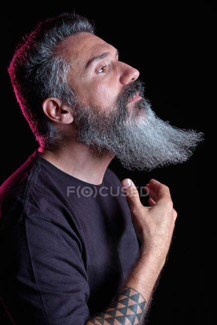 Vue latérale de beau mâle mature avec barbe grise sur fond noir en studio — Photo de stock