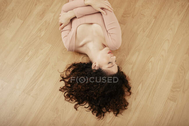 Von oben ein zartes Weibchen im beigefarbenen Body auf Holzboden liegend und mit geschlossenen Augen — Stockfoto