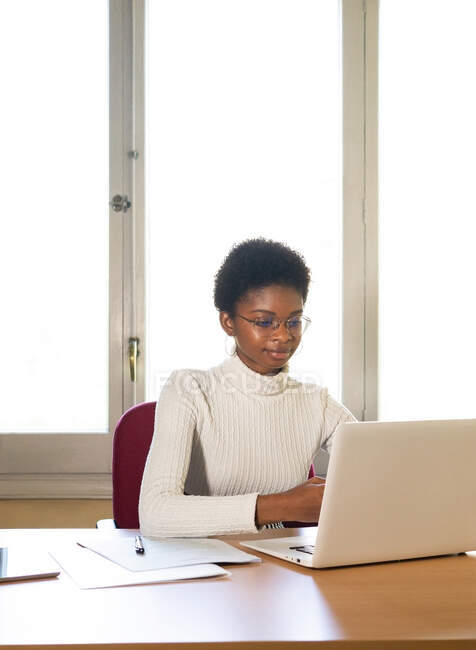 Afroamerikanische Ärztin tippt Bericht auf Laptop, während sie am Tisch in modernem Klinikbüro arbeitet — Stockfoto