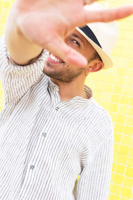 Unbekannter in stylischem Sommeroutfit und Hut macht keine Geste und versteckt Gesicht vor Kamera gegen gelbe Wand — Stockfoto
