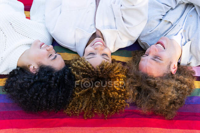 De cima de mulheres diversas e homem com cabelo encaracolado deitado cara a cara em xadrez colorido no parque olhando para cima — Fotografia de Stock