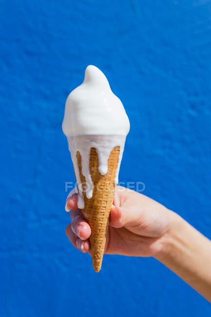 Coltivazione mano di femmina anonima con scioglimento gelato in cono cialda nella giornata di sole su sfondo blu — Foto stock