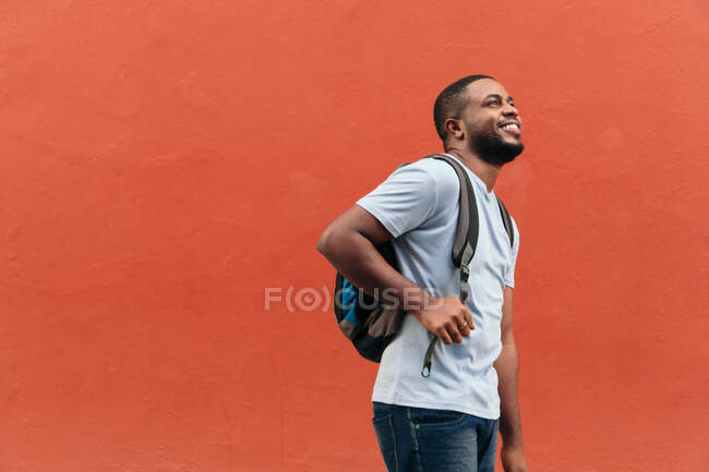 Sorrindo homem negro com mochila olhando para cima, enquanto de pé ao ar livre — Fotografia de Stock