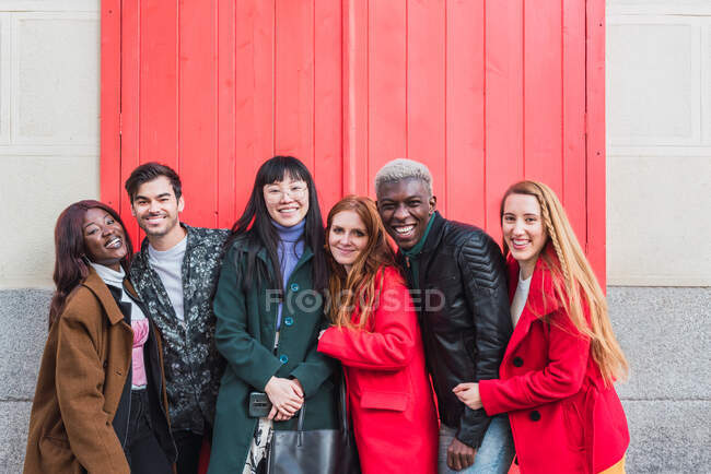 Grupo de amigos multirraciales emocionados divirtiéndose en la ciudad mientras están de pie mirando la cámara en la calle - foto de stock