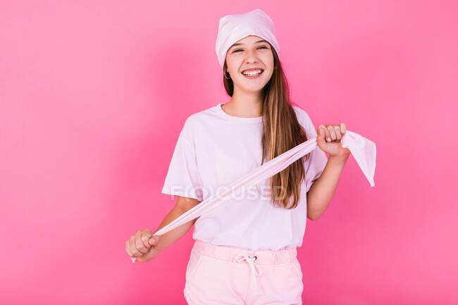 Adolescente donna spensierata in abbigliamento casual con capelli castani e velo che rappresenta la consapevolezza del concetto guardando lontano in piedi su sfondo rosa — Foto stock